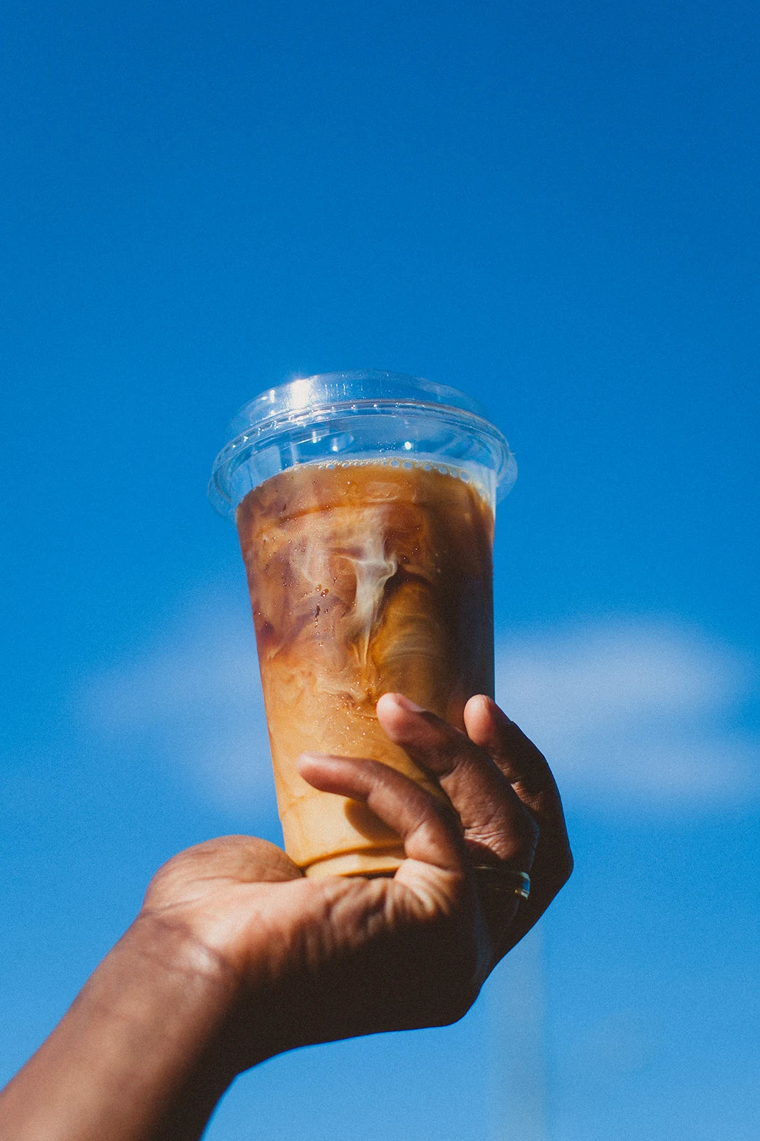 A hand raises an iced Wake Up coffee into a bright blue summer sky